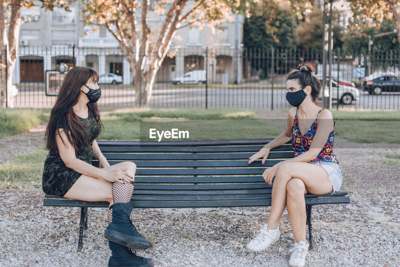Full length of women wearing mask sitting on bench in park