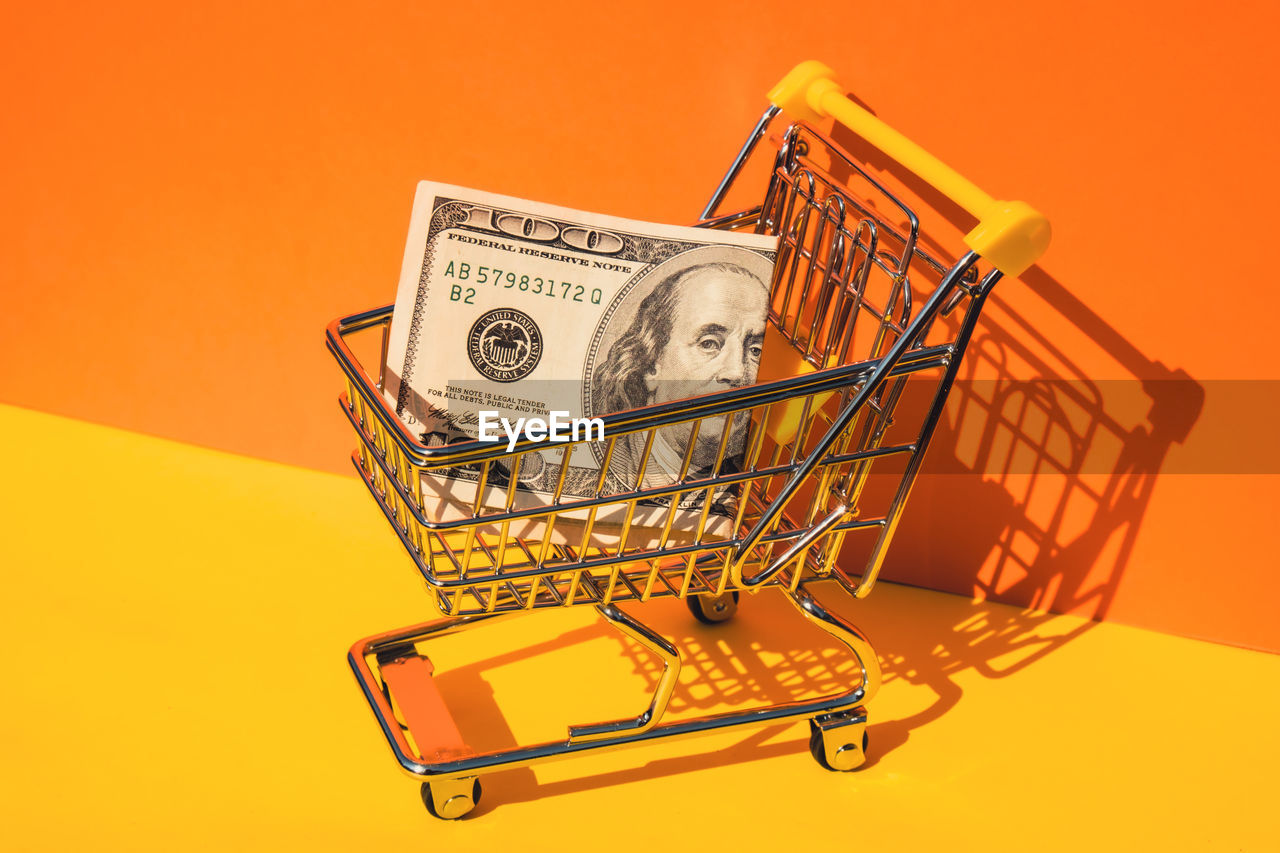 Us dollar paper currency 100 banknote money shopping trolley cart on colorful orange yellow