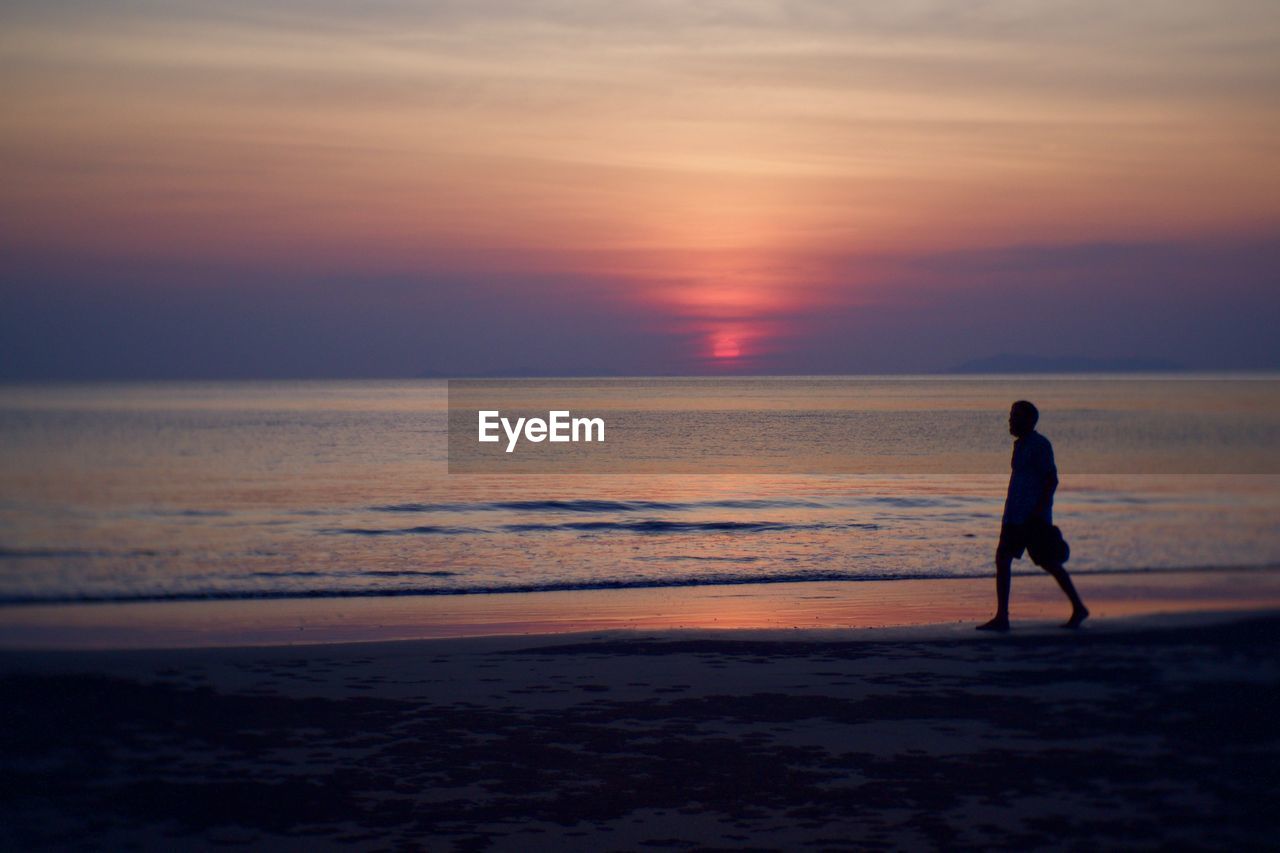 SILHOUETTE MAN WALKING ON BEACH DURING SUNSET