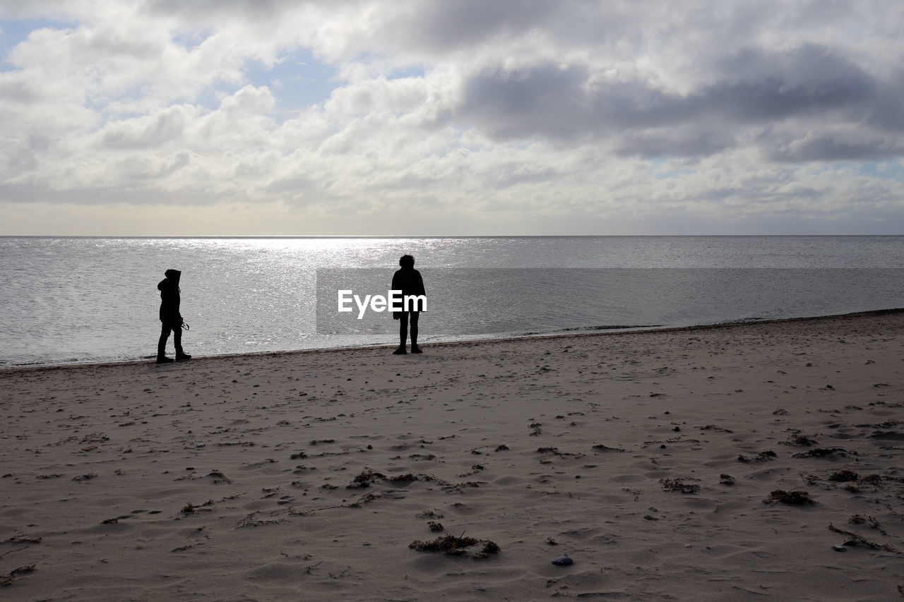 SILHOUETTE MEN STANDING AT BEACH AGAINST SKY