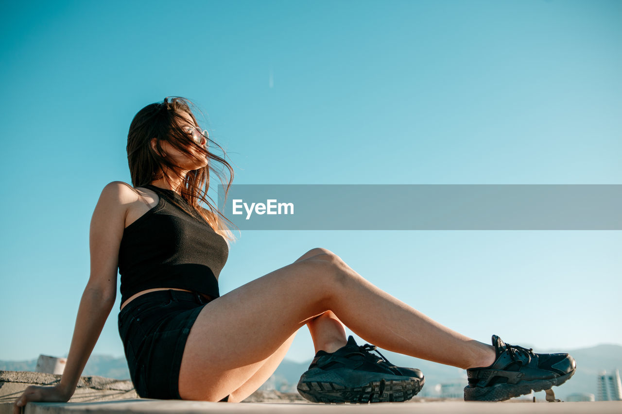 Side view of girl sitting against sky