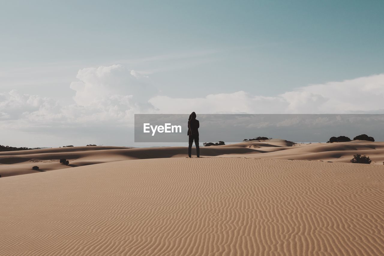 Rear view of man standing on sand dune in desert against sky