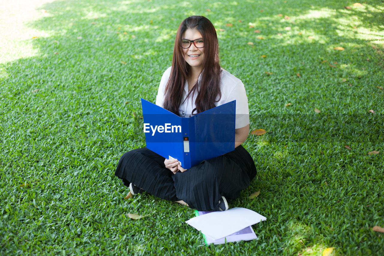 Portrait of young woman with file and papers sitting on grass