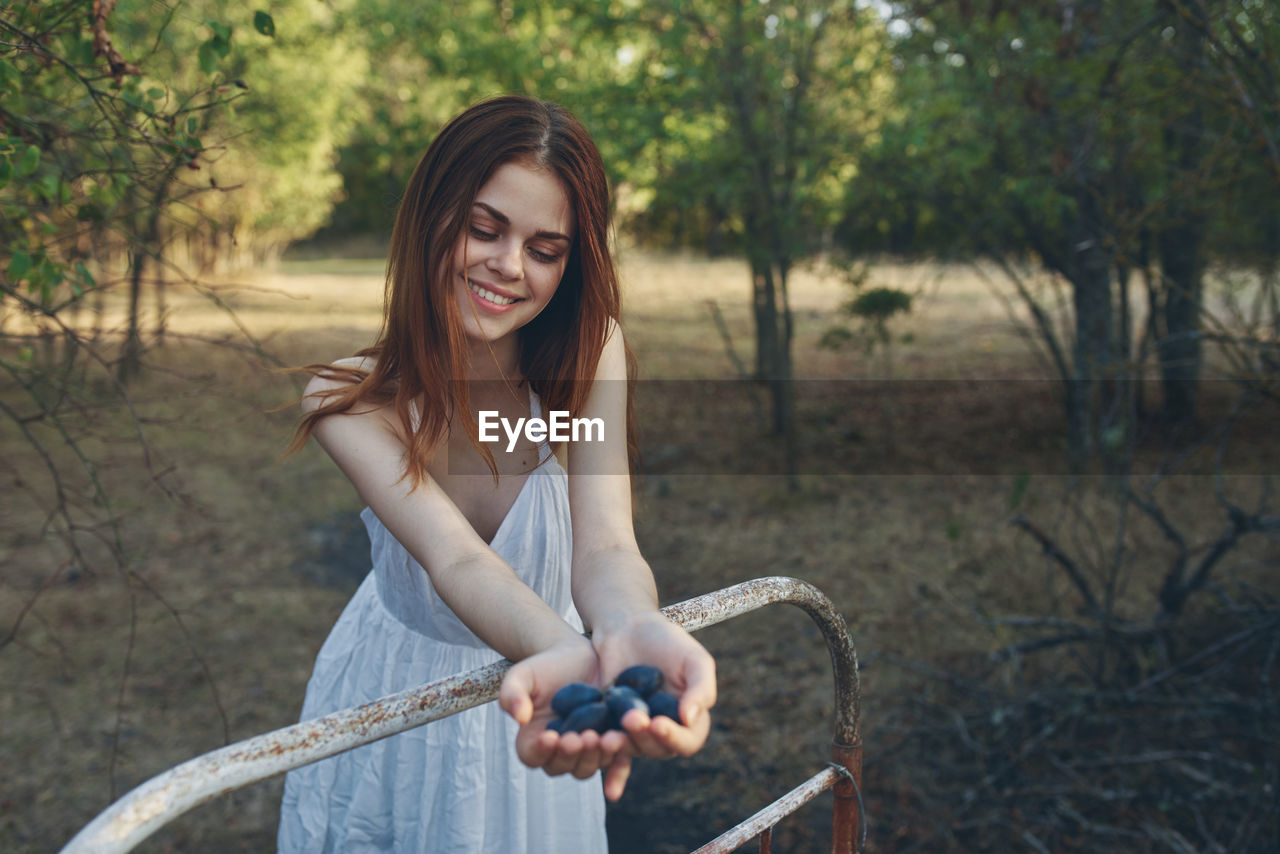 Young woman smiling while holding plants against trees