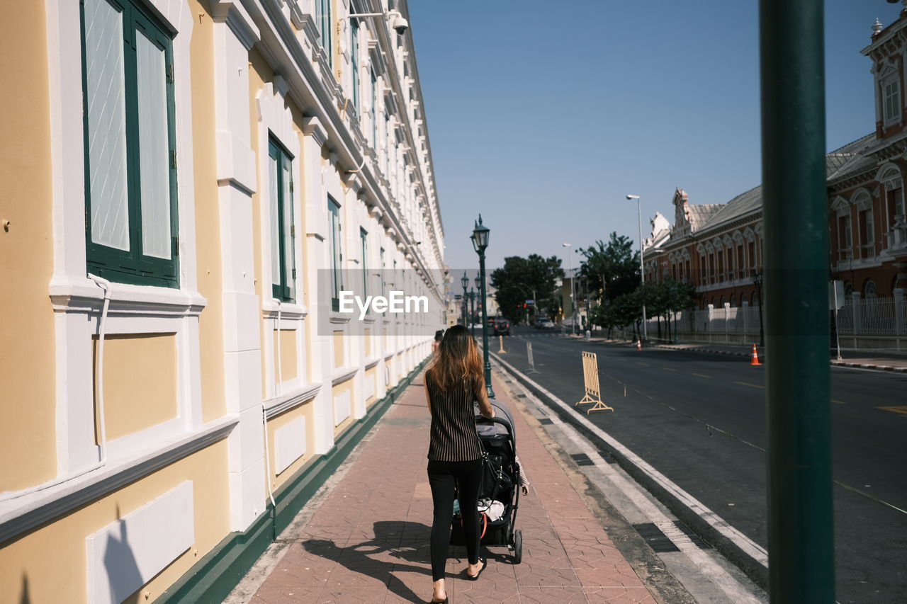 REAR VIEW OF WOMAN WALKING ON STREET AMIDST BUILDINGS