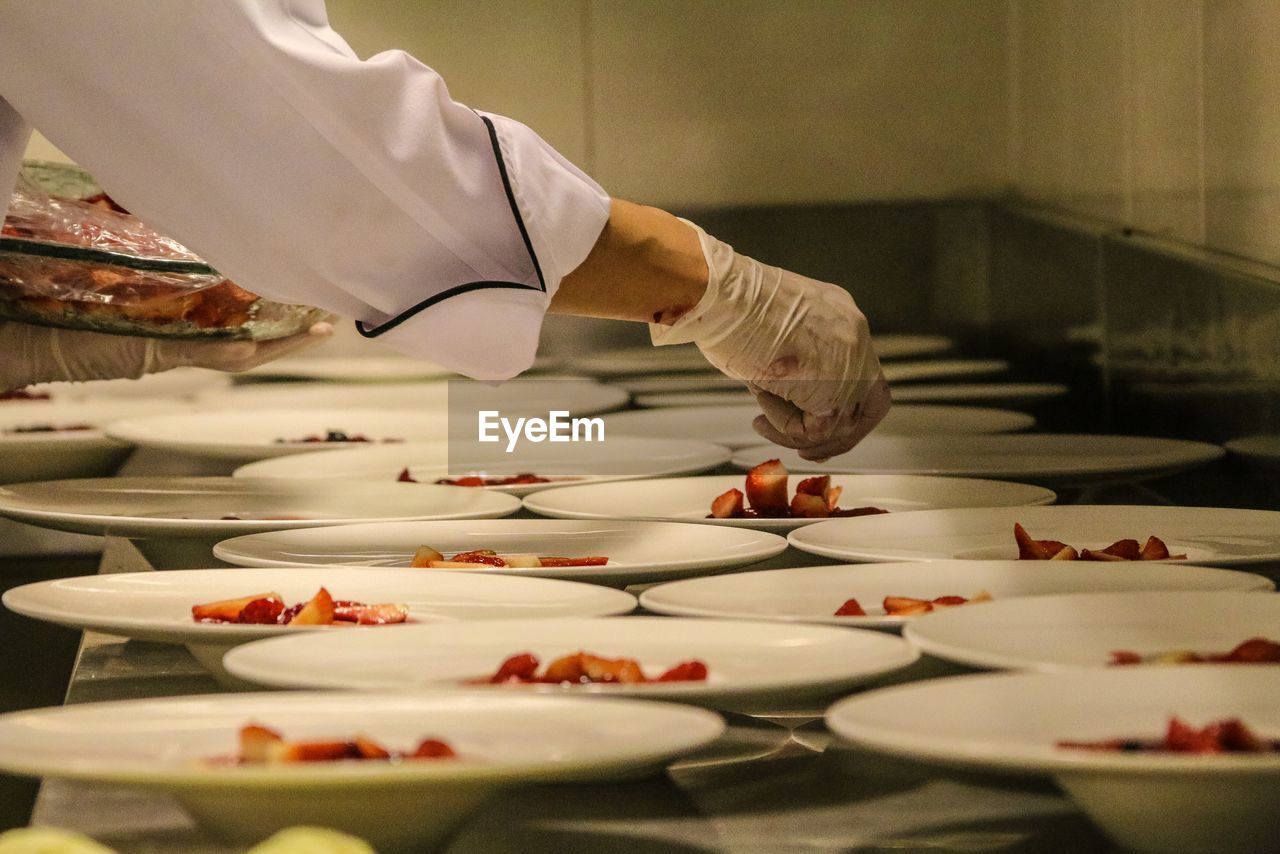 Cropped hand of chef arranging dessert on plates at kitchen