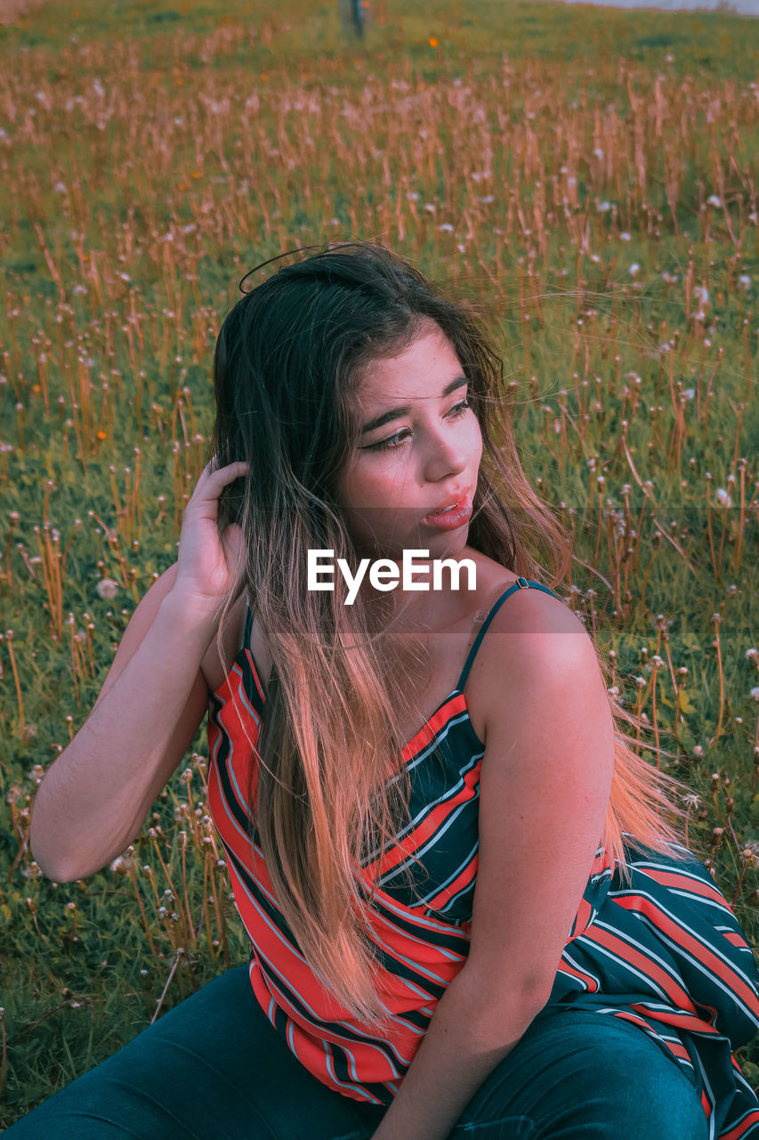 Young woman looking away while sitting on land