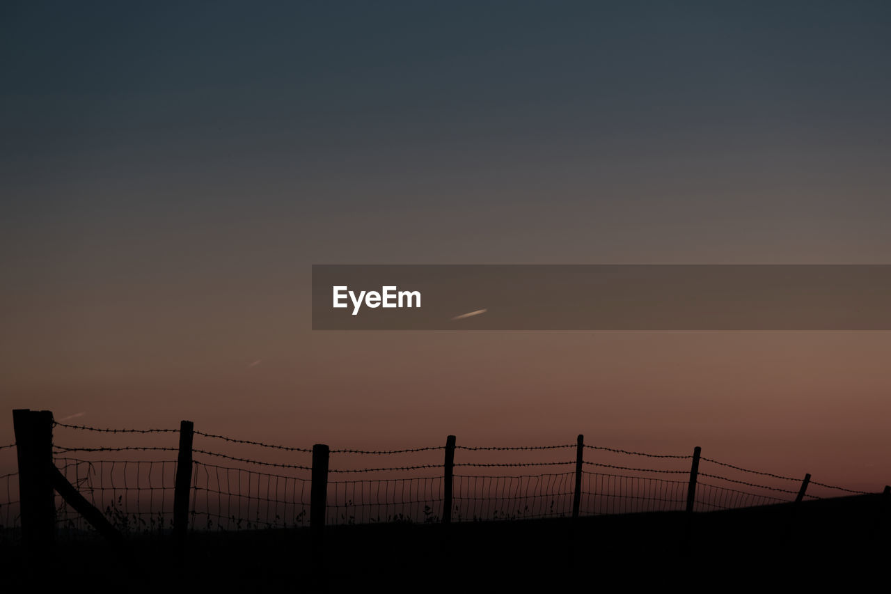 Vapour trails of airplanes at sunset. a silhouette of a barbed wire fence on a hill.