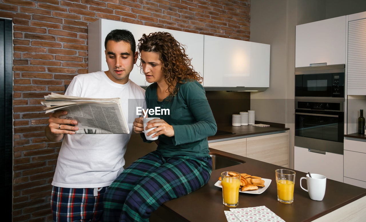 Full length of couple reading newspaper in kitchen