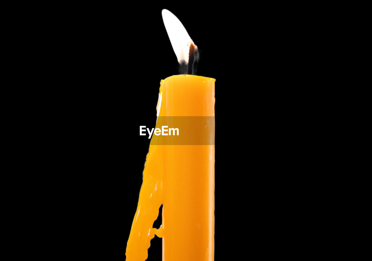 CLOSE-UP OF YELLOW CANDLE ON BLACK BACKGROUND