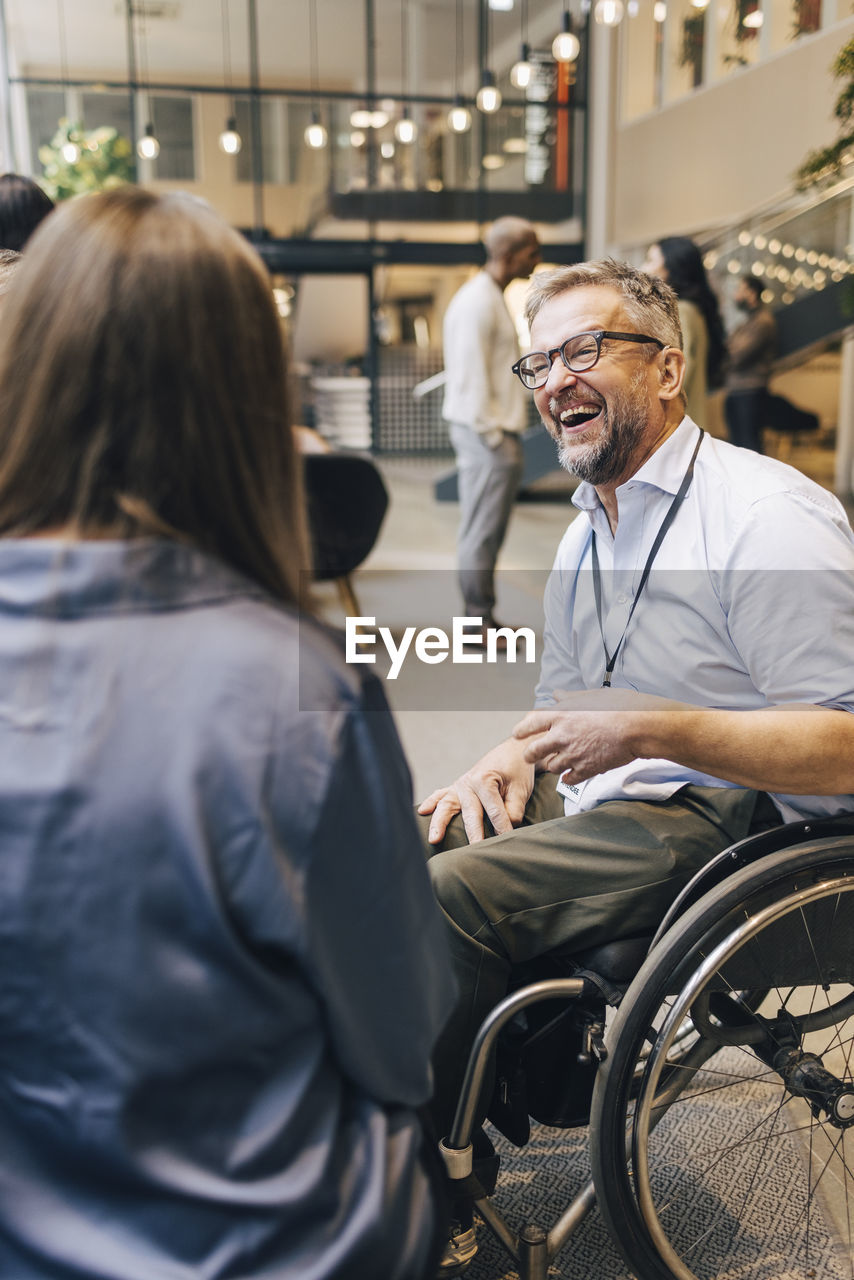 Happy male entrepreneur with disability sitting on wheelchair during networking event at convention center