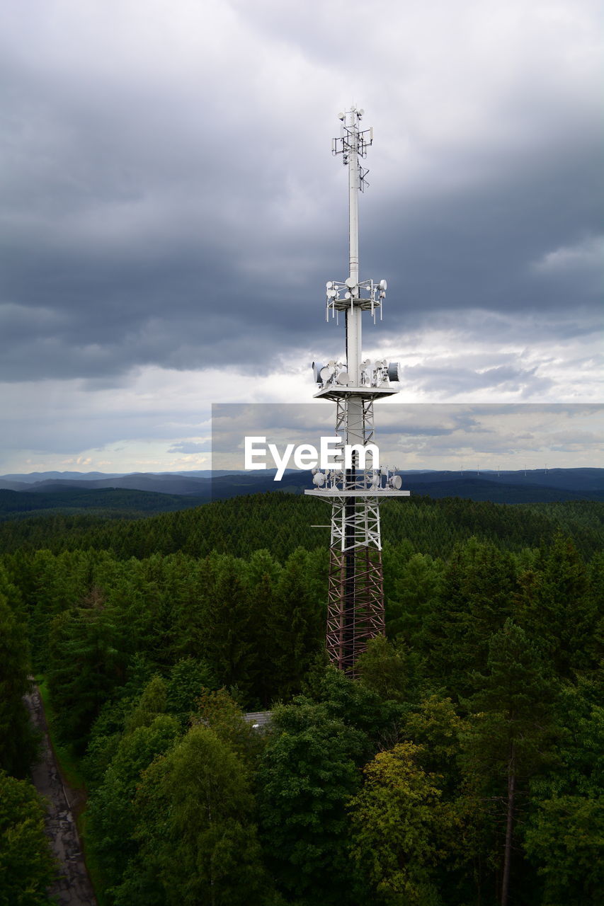 Communications tower amidst trees against cloudy sky