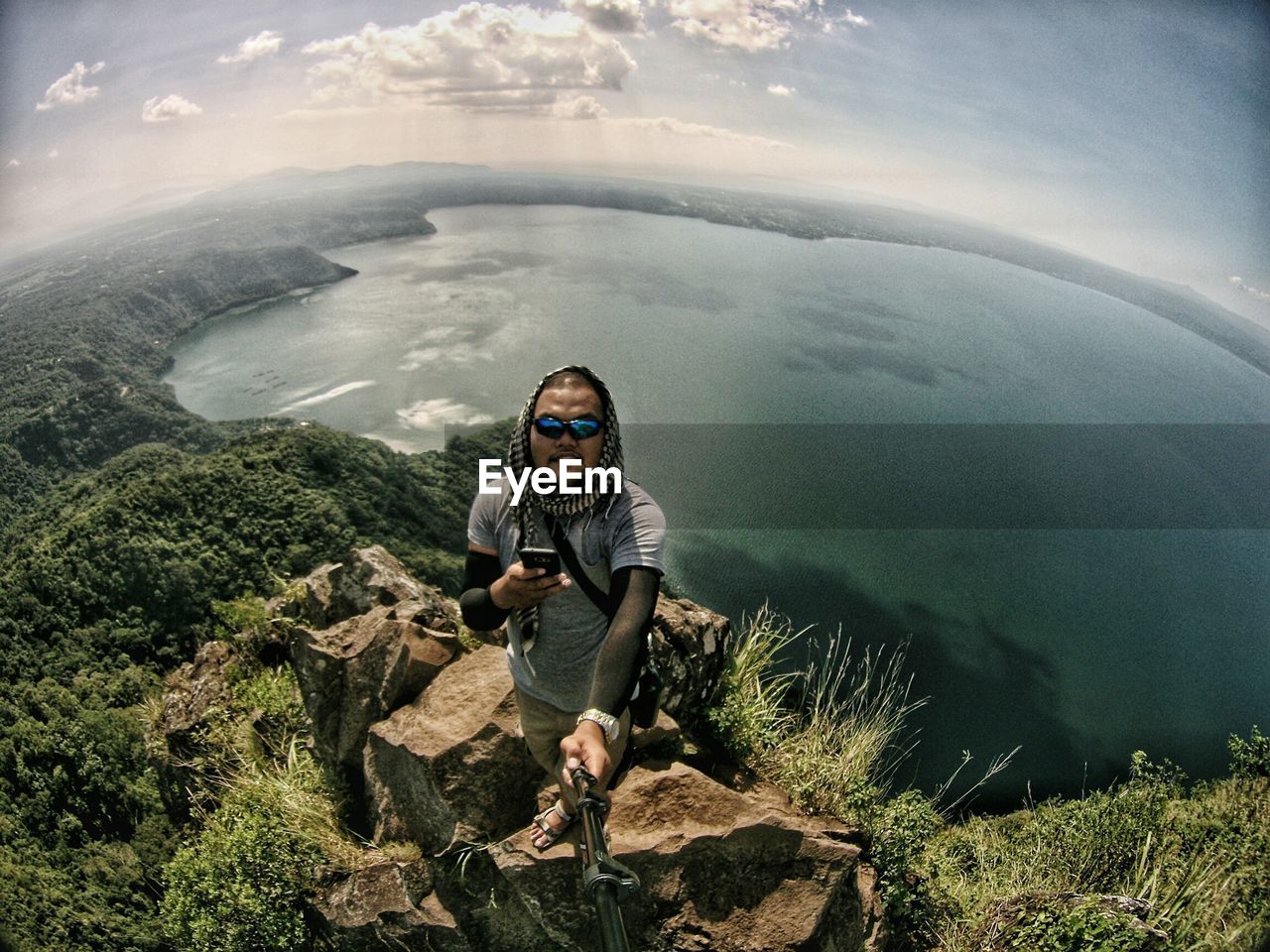 High angle view of man holding monopod while standing on rock against sea