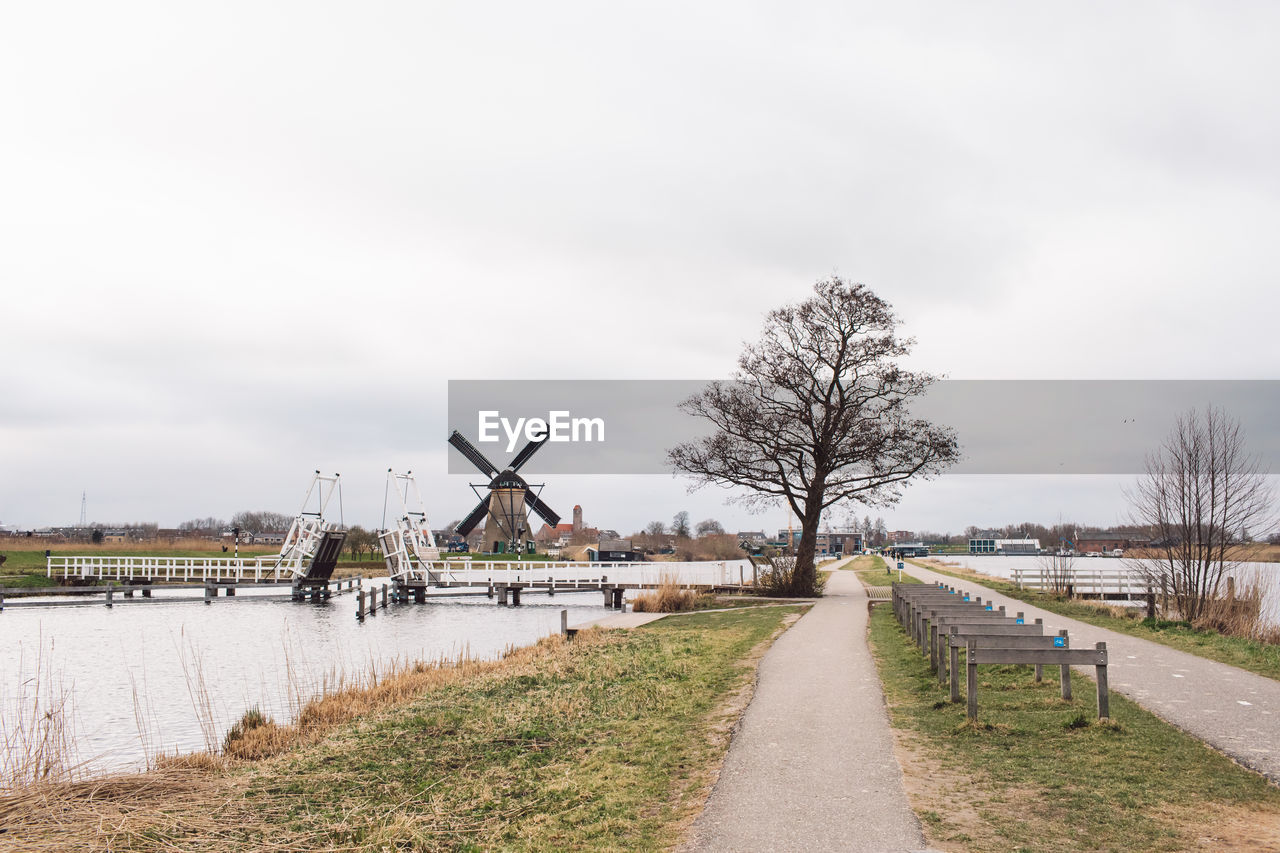 Traditional windmill by canal against sky