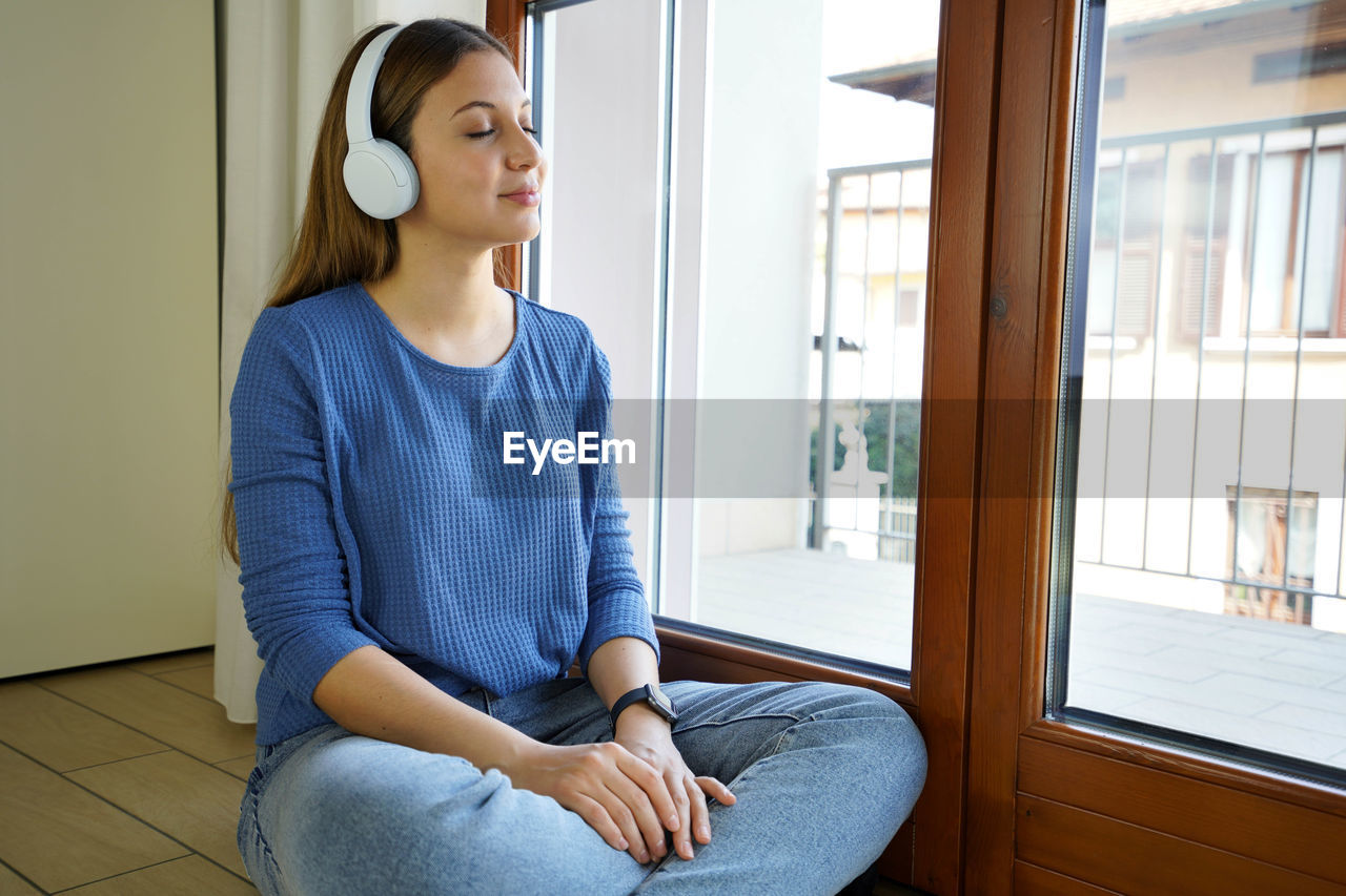 Smiling woman listening music while sitting by window