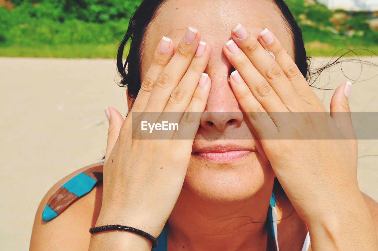 Close-up of woman with hands covering eyes at beach on sunny day