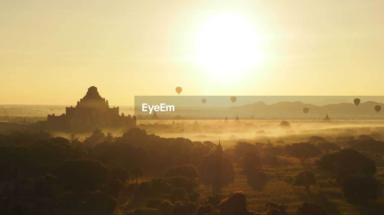 Hot air balloons over silhouette temples against sky during sunrise