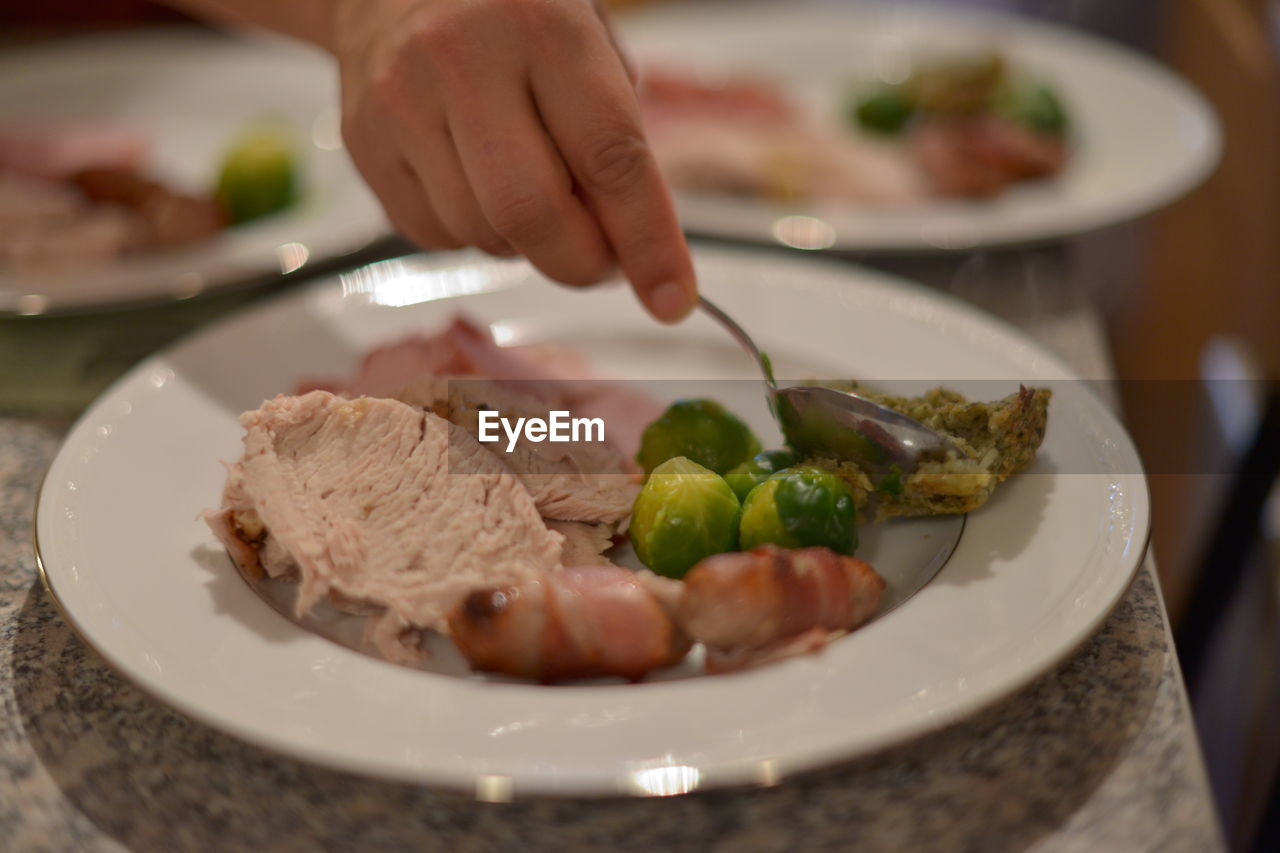 Cropped image of hand holding spoon over food in plate