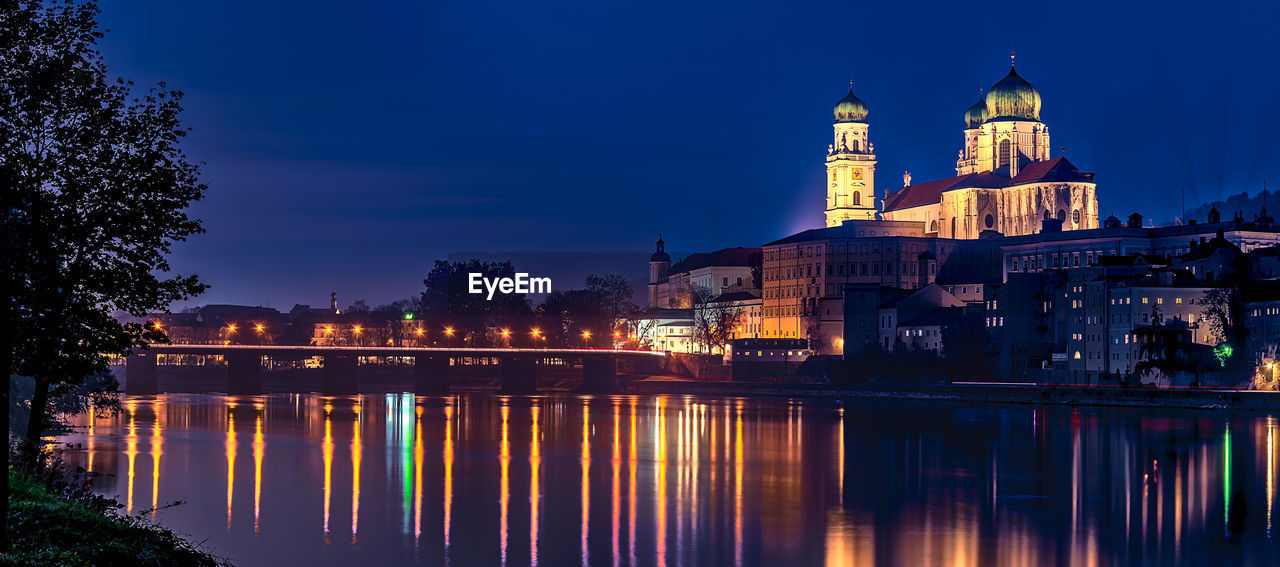 Reflection of illuminated buildings in river against sky at dusk