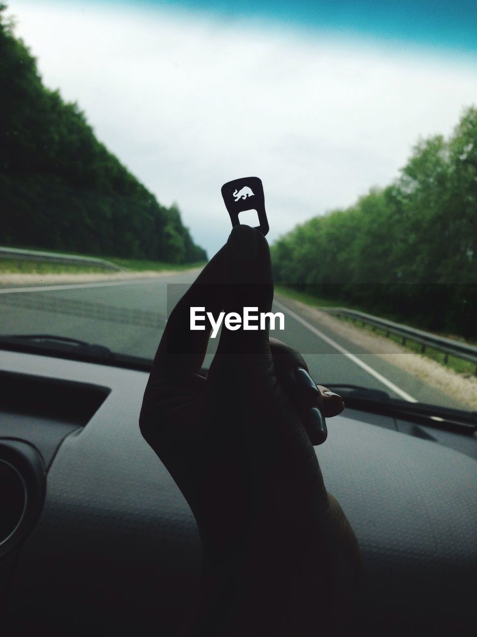 Cropped image of person holding can tab while sitting in car against sky