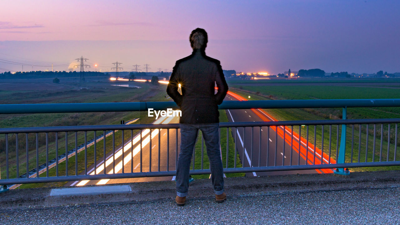 Rear view of man standing on bridge above light trails