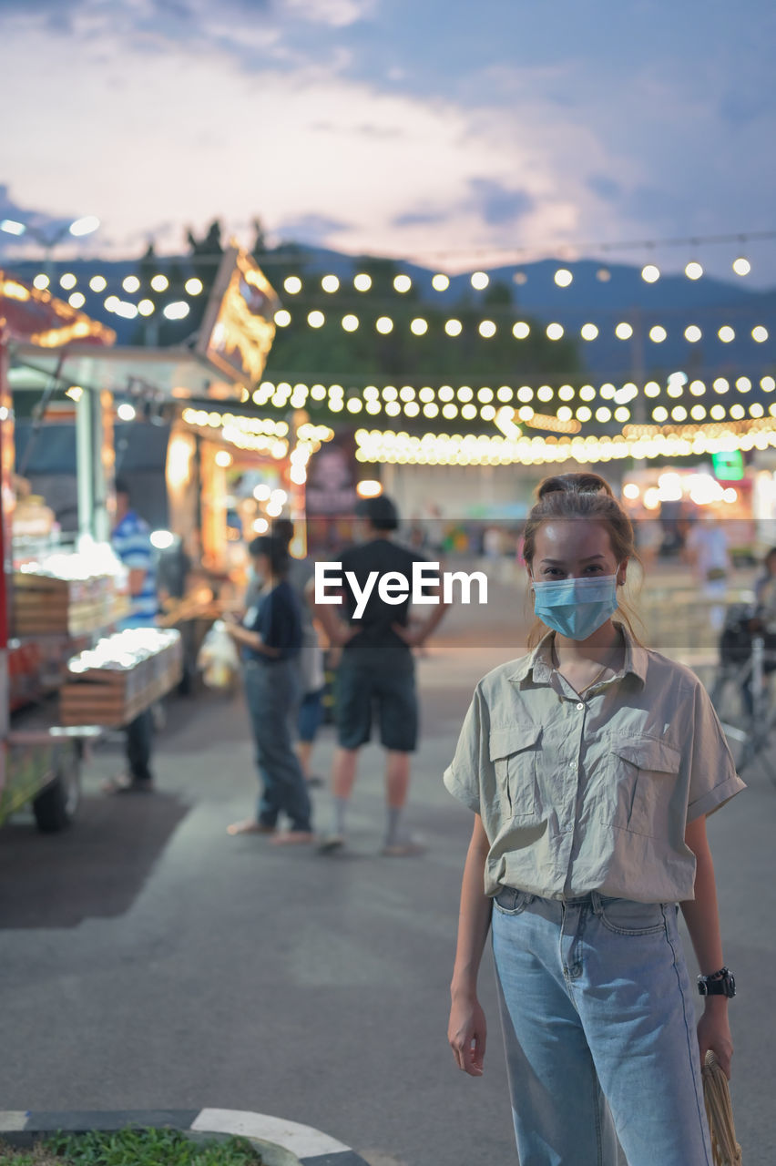 Young women wearing surgical mask standing in night market , chaing mai , thailand