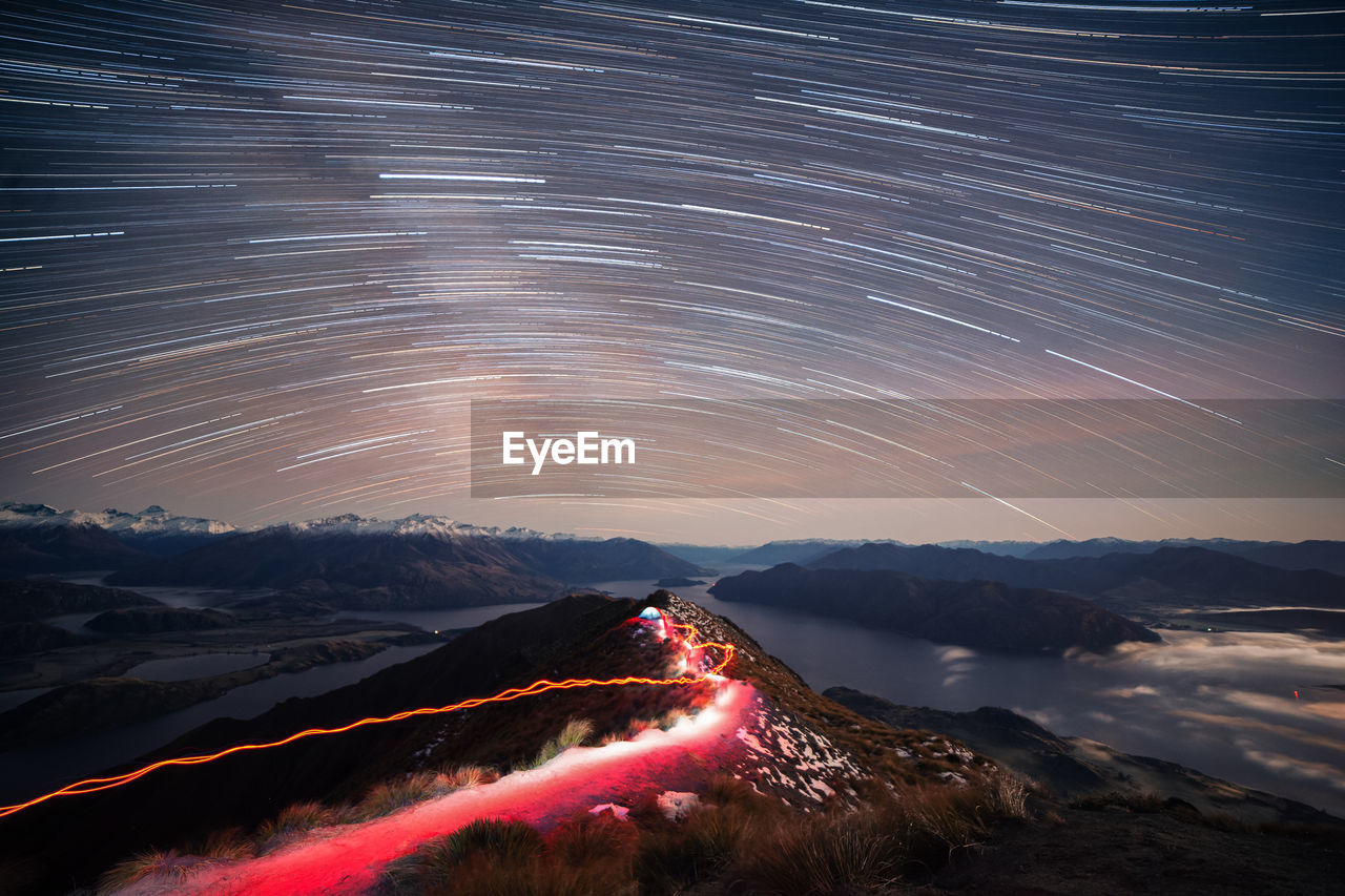 Star trails over landscape against sky at night