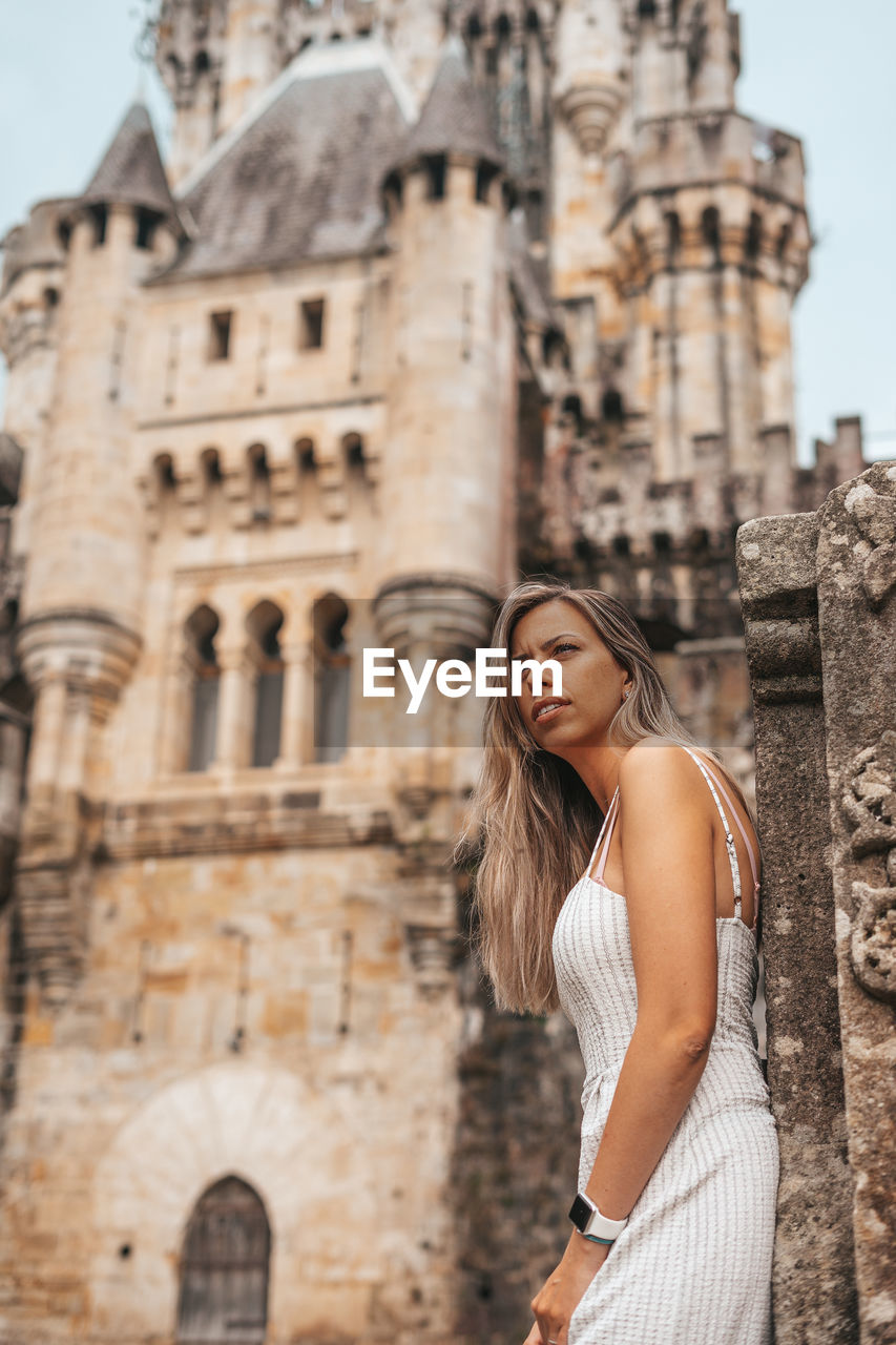 Young woman looking away while standing against historic building