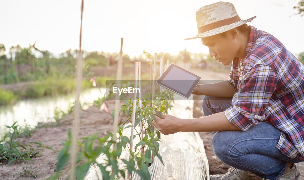 Young farmer using digital tablet examining plants at agriculture field