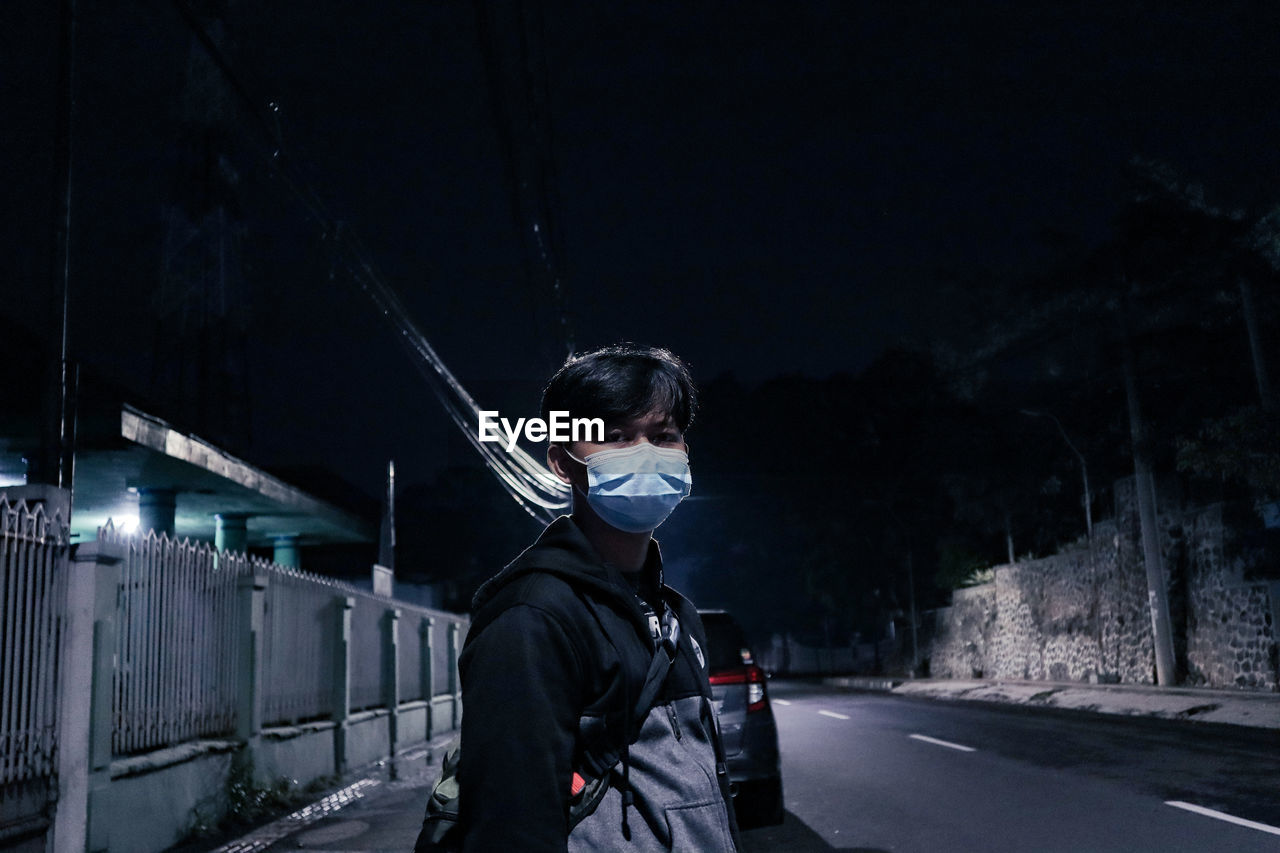 Portrait of young man standing on illuminated road during winter