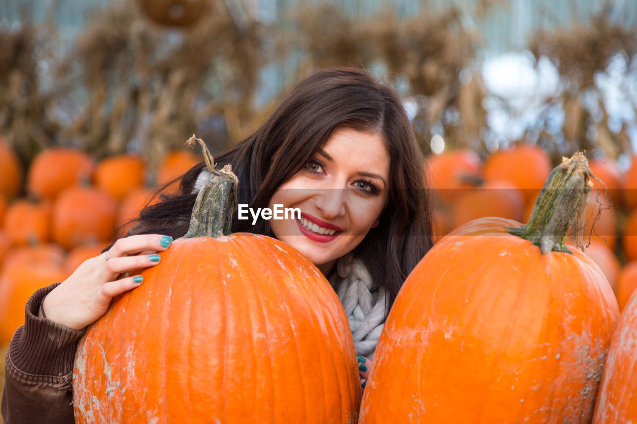 PORTRAIT OF A SMILING YOUNG WOMAN WITH PUMPKINS IN BACKGROUND
