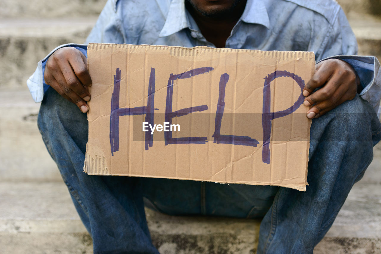 Midsection of beggar holding cardboard with text