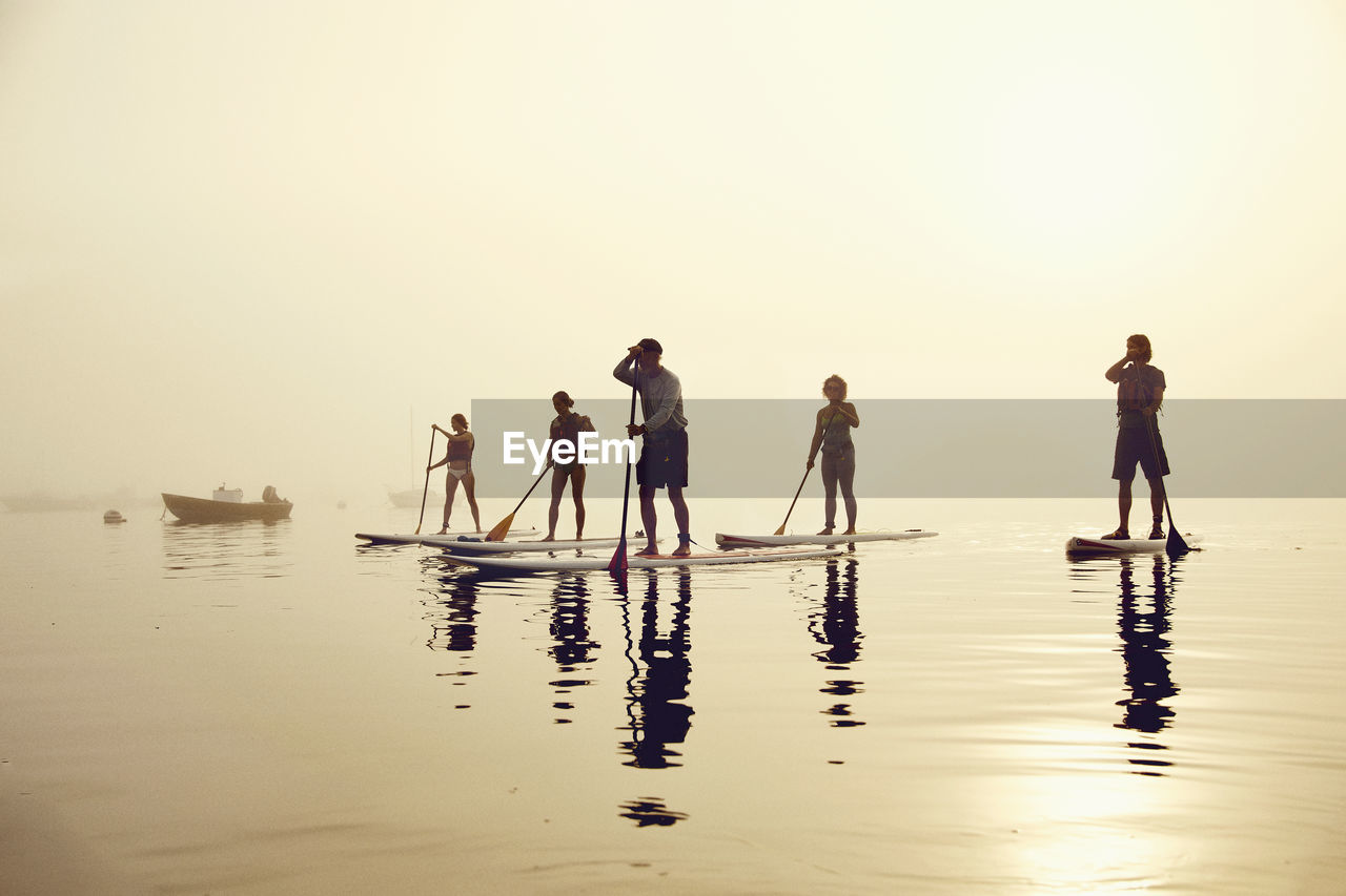 A group of standup paddle boarders on a foggy morning at sunrise