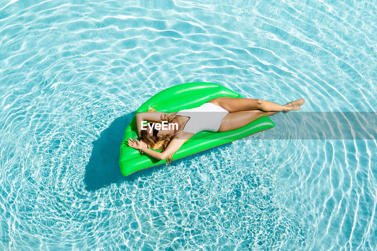 From above full body smiling female in white one piece suit chilling on air mattress on pool water on hot sunny day