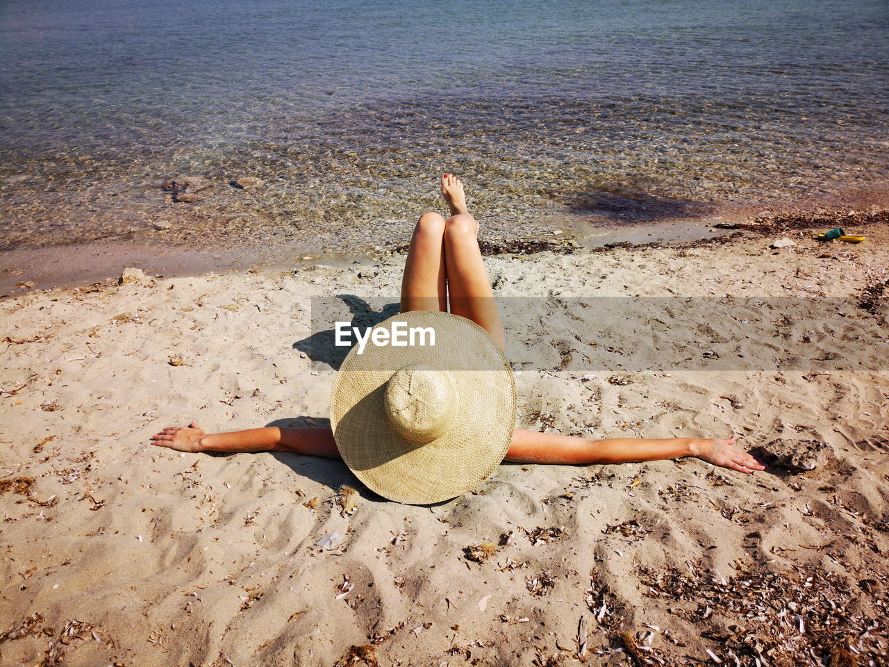 Mature woman lying on a sand beach her head covered with hat