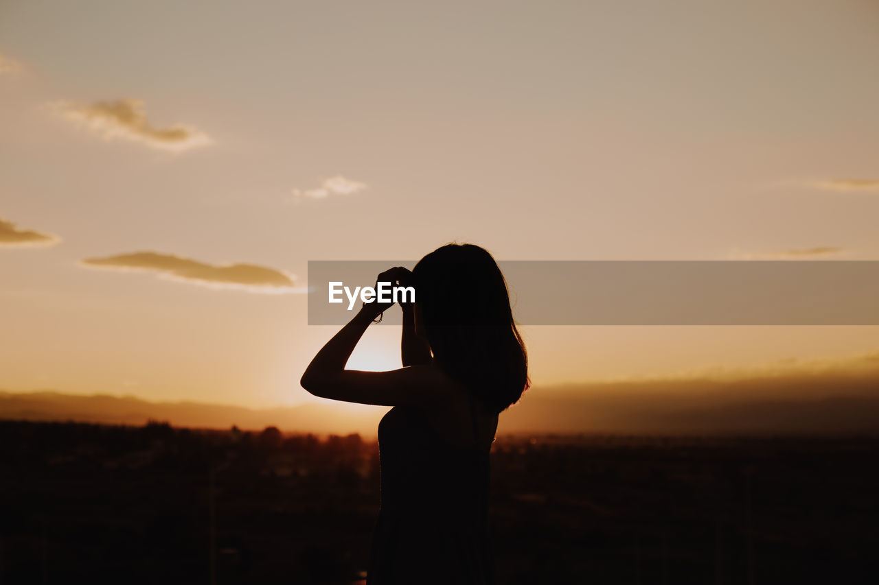 Mature woman standing on terrace against sky during sunset