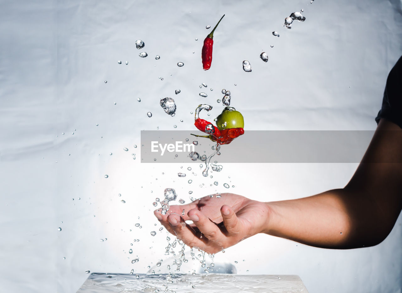 Close-up of hand splashing water with red chili peppers and olive