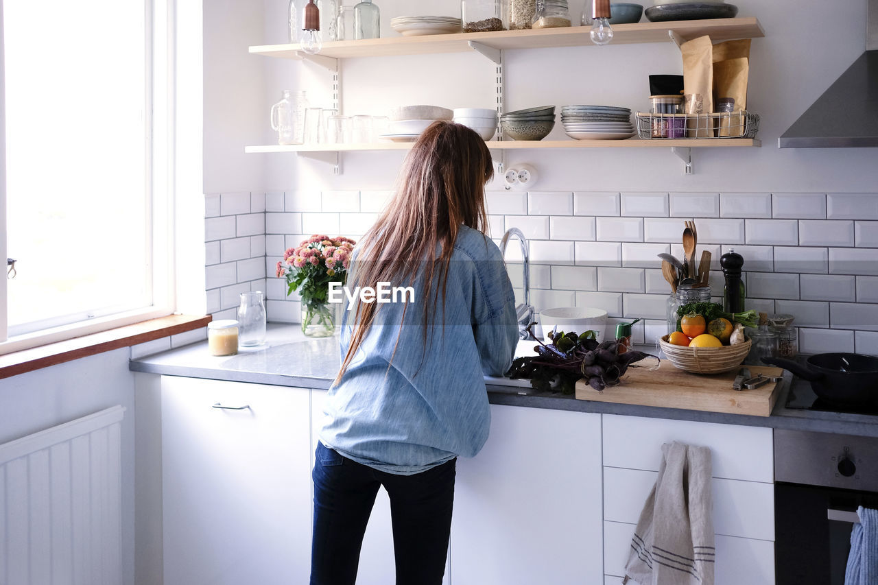 Rear view of woman cooking by window in kitchen