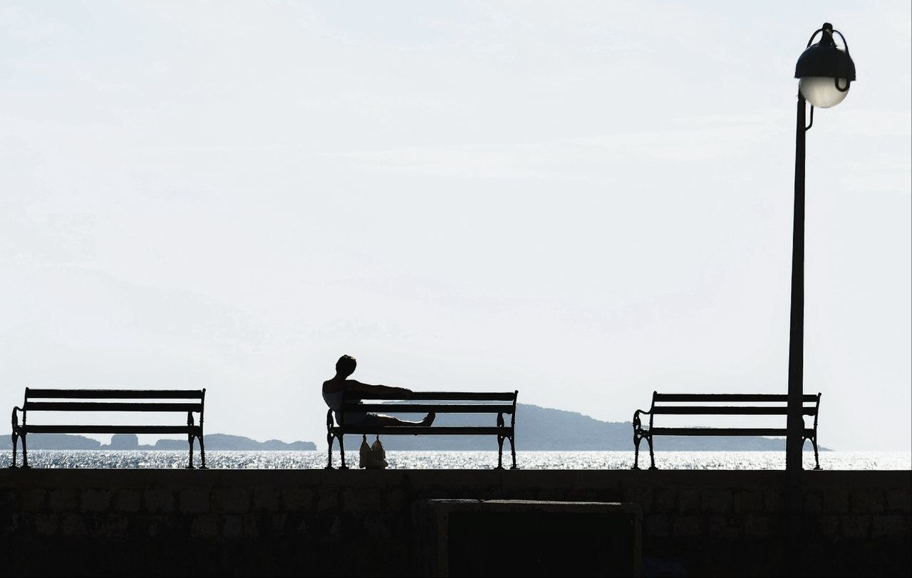 Silhouette of person sitting on bench at seaside