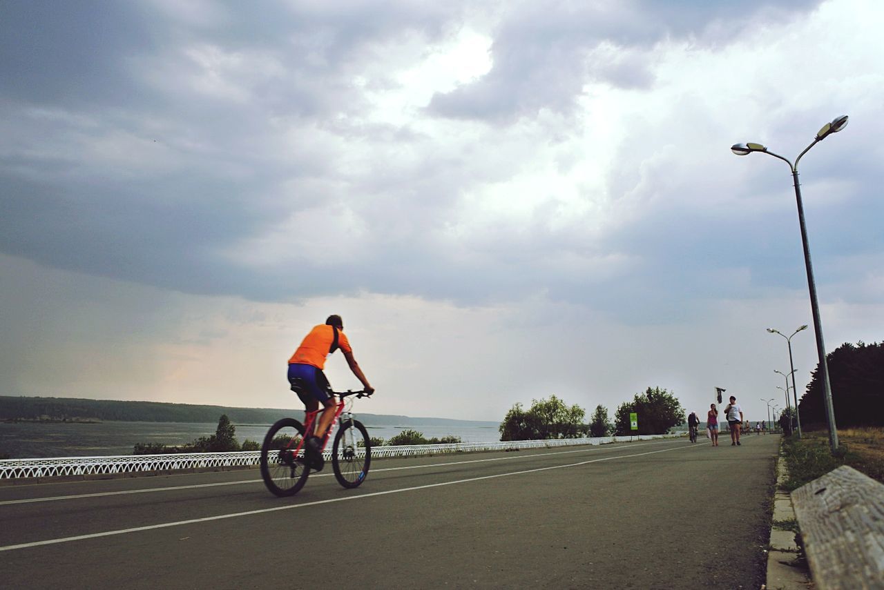 PERSON RIDING BICYCLE ON ROAD AGAINST SKY