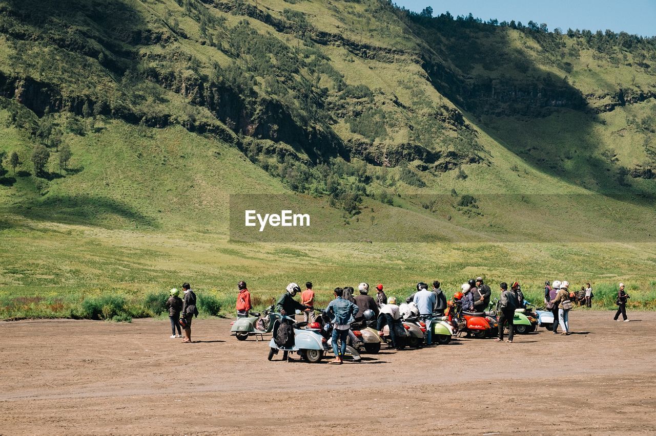 People with motor scooter on field against mt bromo