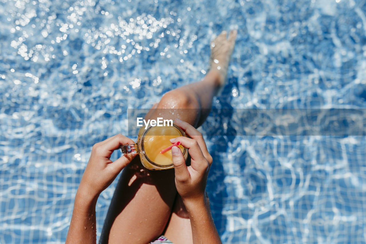 Low section of woman having drink in swimming pool