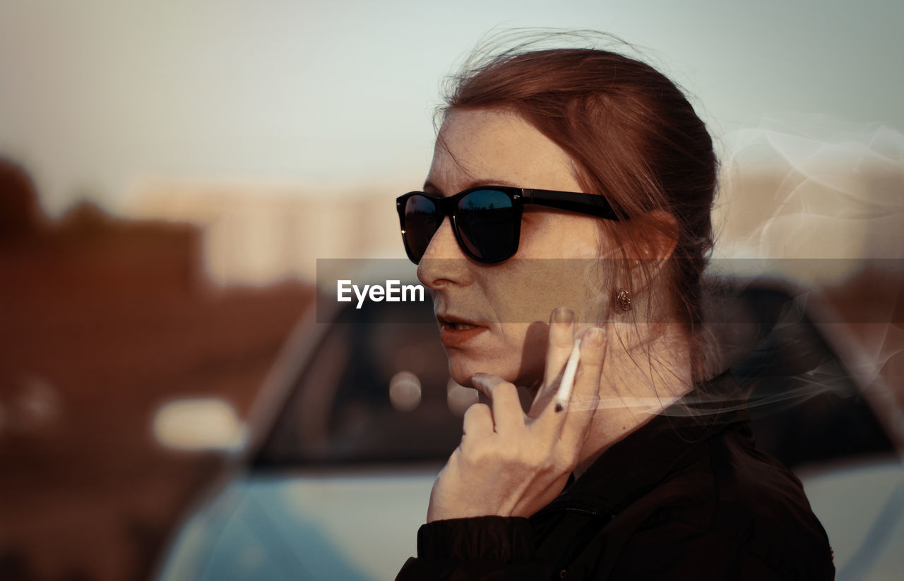 Young woman smoking cigarette while wearing sunglasses