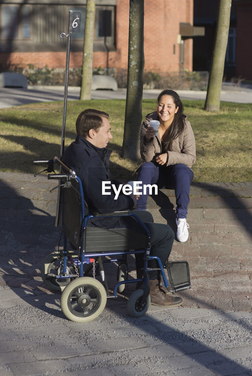 Young woman and man on wheelchair having coffee break