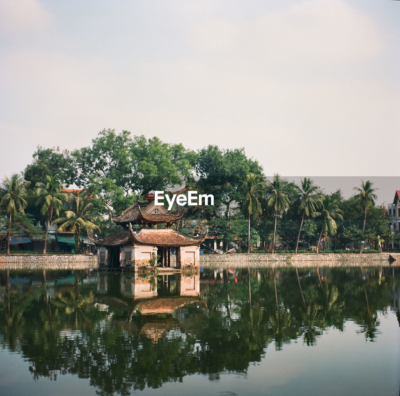 Reflection of house and trees by lake against sky