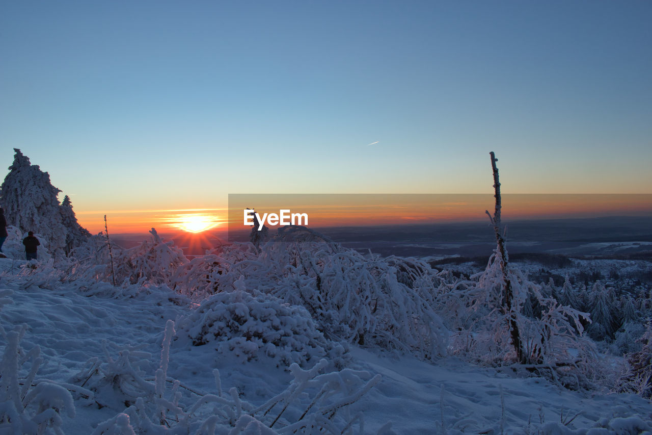 SNOW COVERED LANDSCAPE AGAINST SKY AT SUNSET