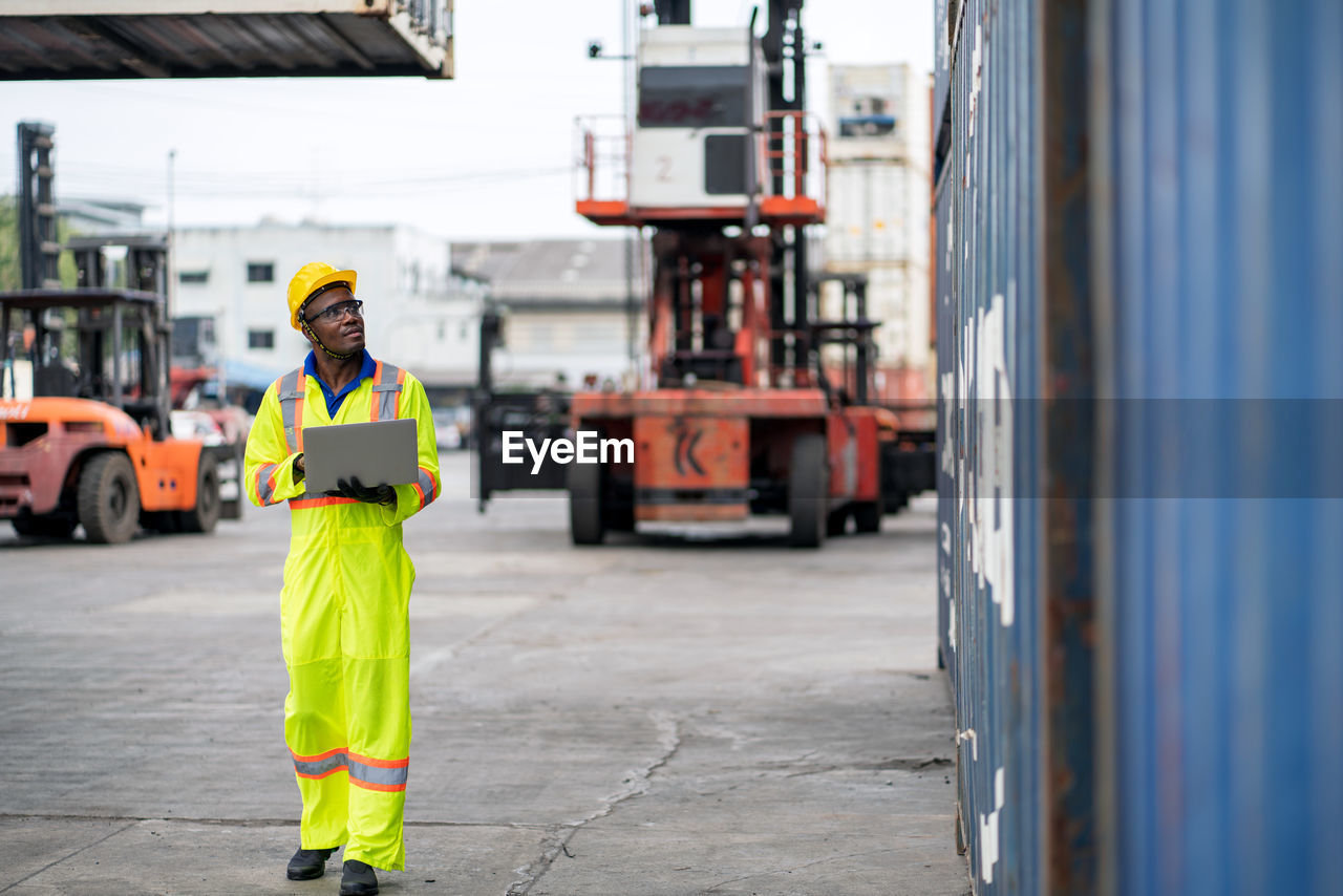 Engineer using laptop while analyzing cargo containers at harbor