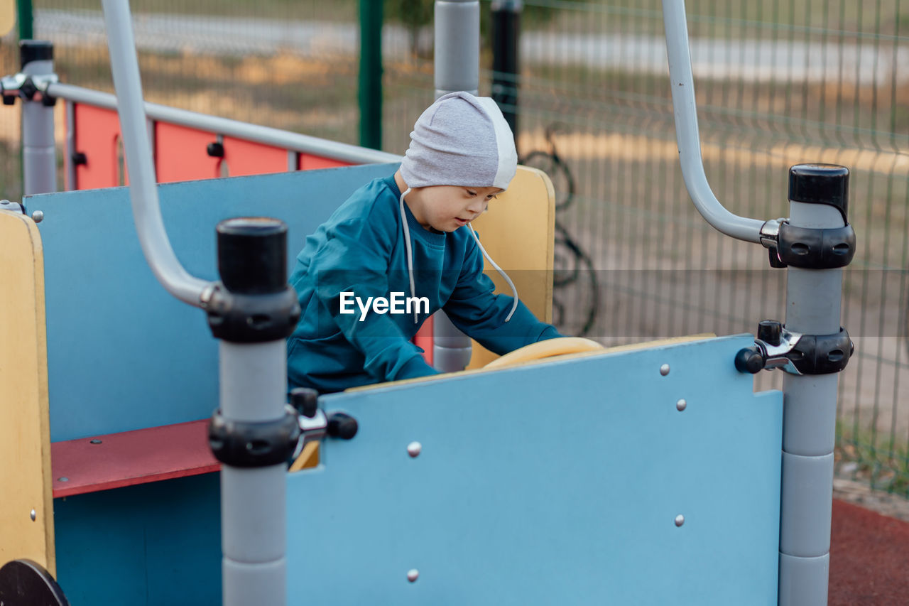 Cute little boy with down syndrome in a funny hat walks in the playground