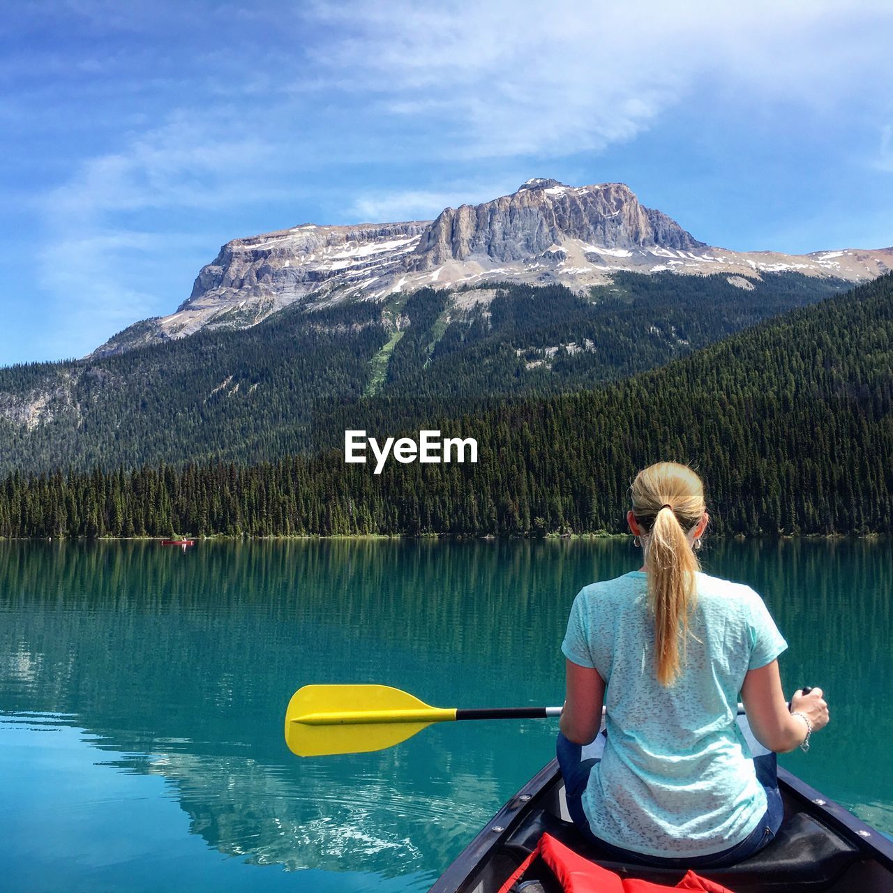 Rear view of woman sitting on canoe in lake against mountain