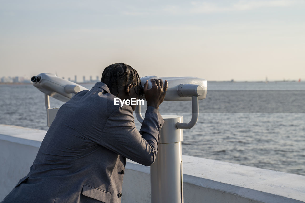 Businessman looking through coin-operated binoculars at sunset